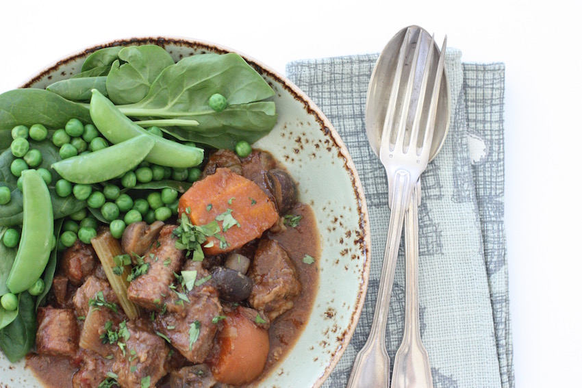 A bowl of slow cooker beef and sausage casserole with cutlery and a napkin