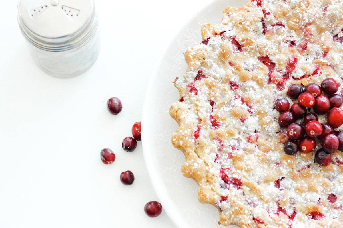 Cranberry and Walnut Tart on a white plate with an icing sugar shaker