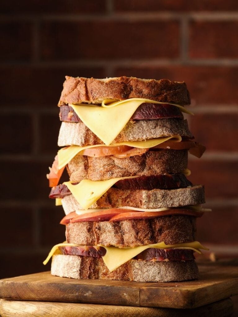 A tall ham and cheese sandwich against a brick wall