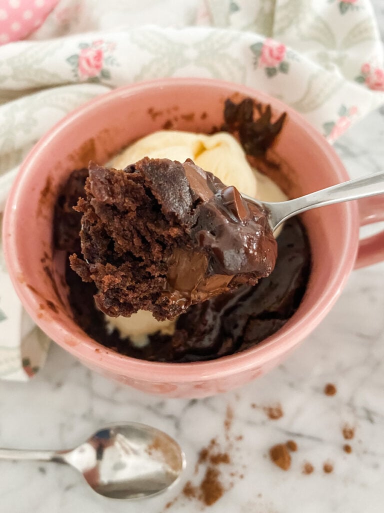Chocolate cake in a pink mug overhead shot with a spoonful of cake and melting ice cream