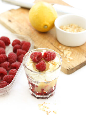 easy lemon and raspberry cheesecake in a glass in front of a wooden chopping board