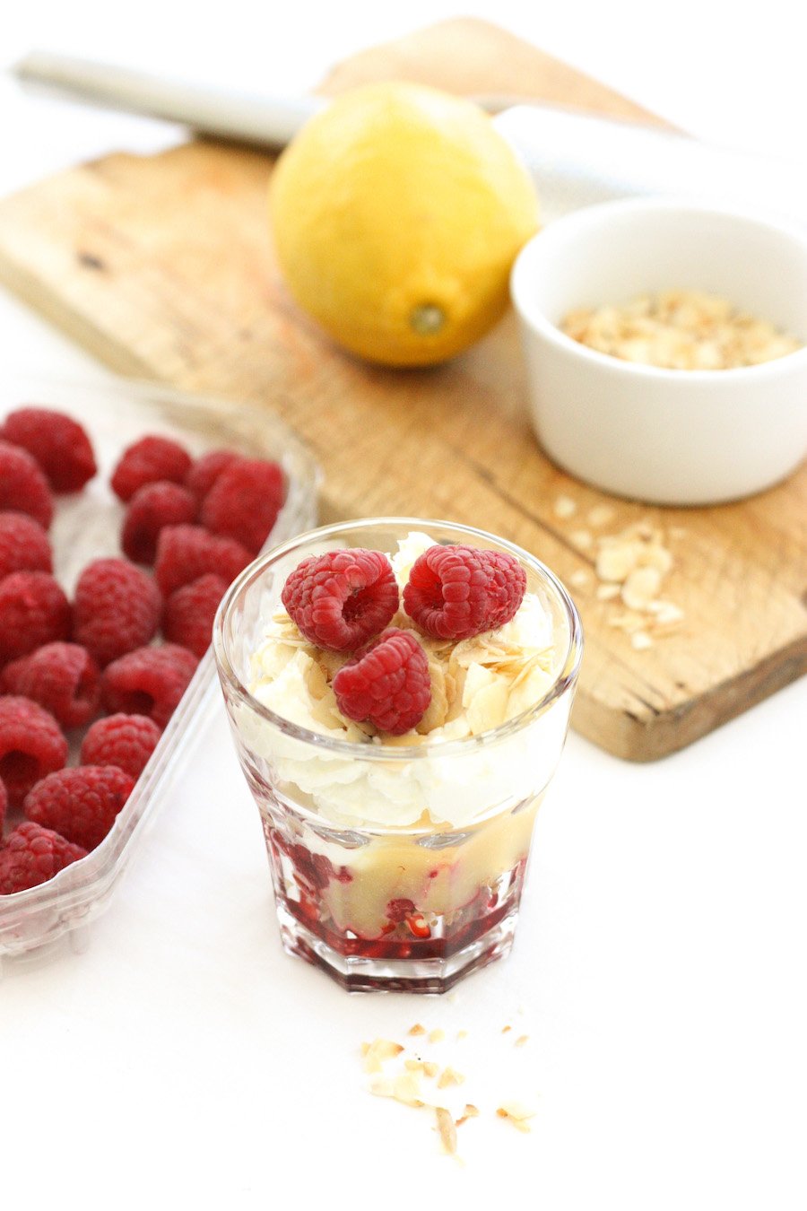 An Easy Lemon and Raspberry Cheesecake in front of a chopping board and a carton of raspberries