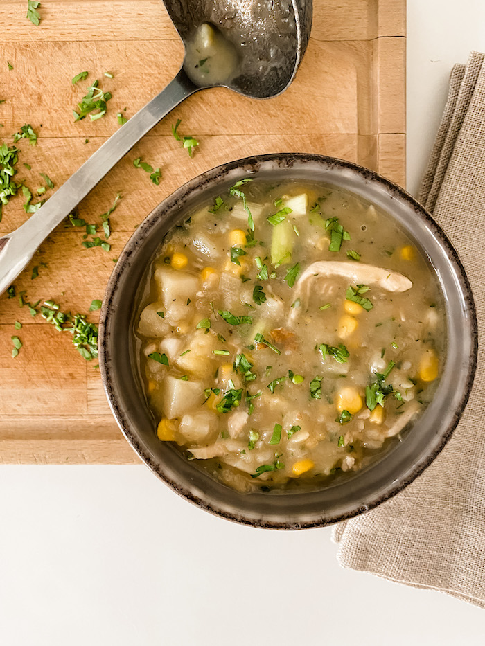 A bowl of chicken and sweetcorn chowder with a ladle on a wooden board