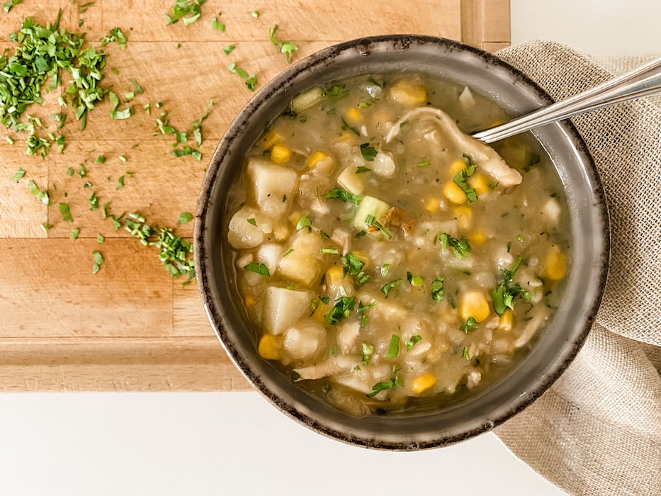 A bowl of chicken and sweetcorn chowder with a spoon on a wooden board
