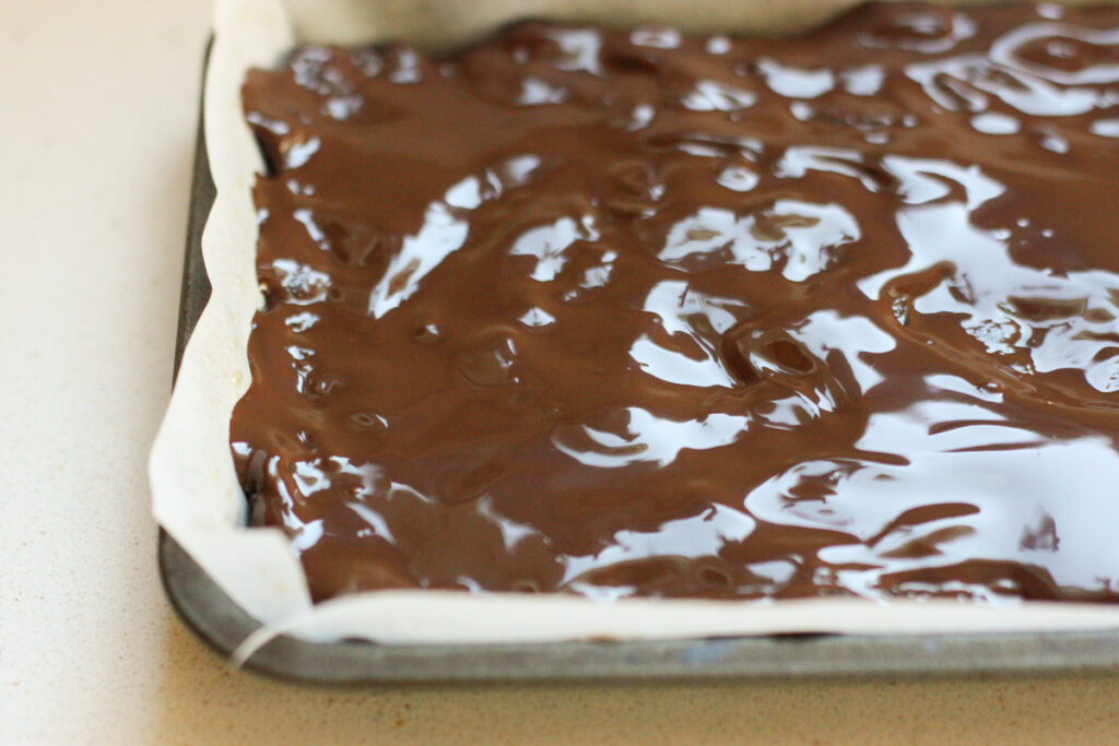 Melted chocolate cooling on the top of chocolate tiffin in a tray