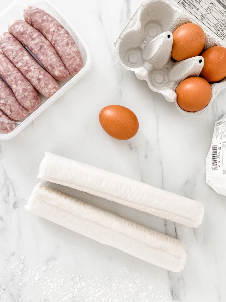 Ingredients for easy homemade sausage rolls - sausages, puff pastry, flour and an egg
