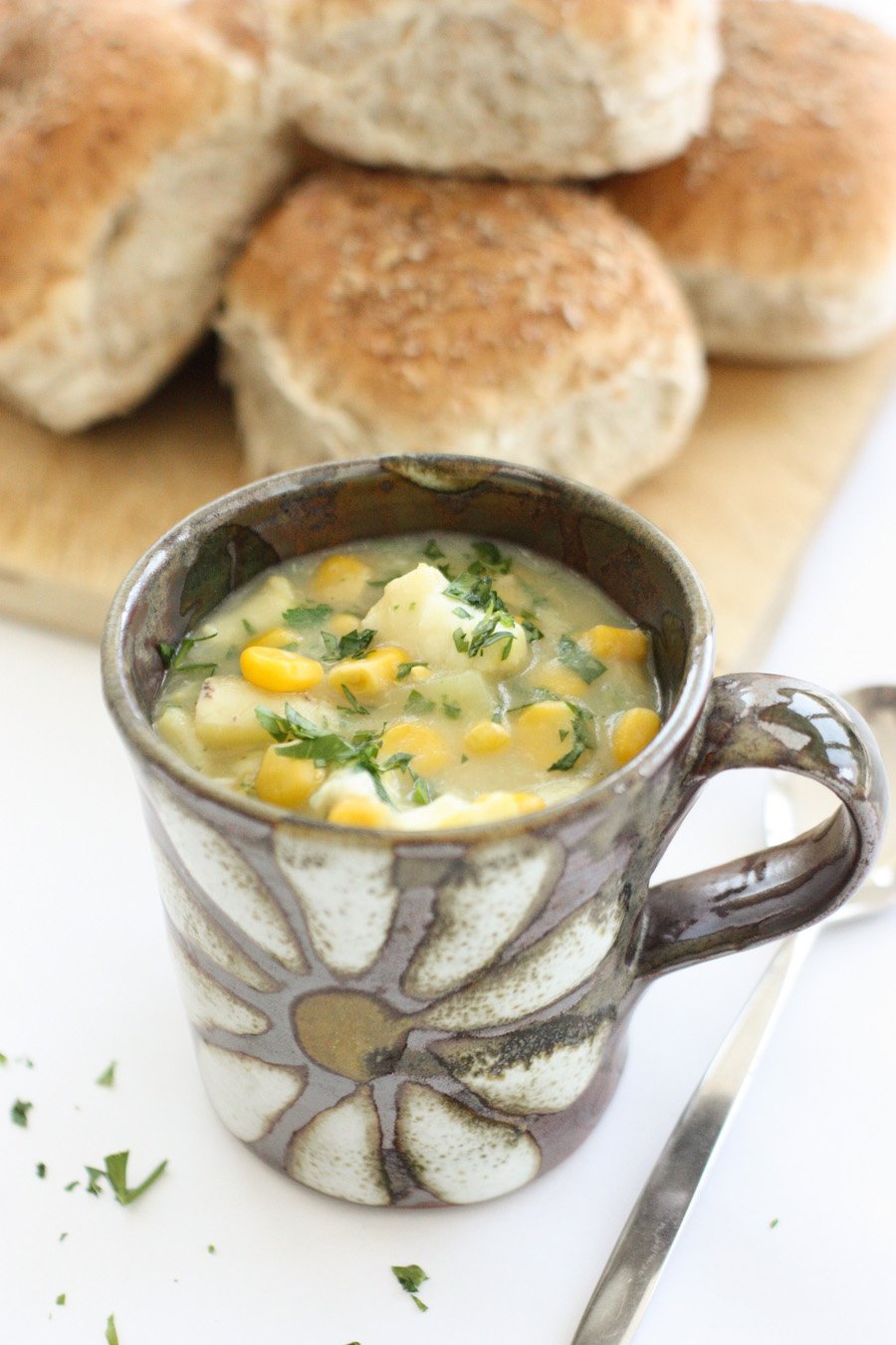 Smoked haddock and sweetcorn chowder in a small brown mug with brown rolls in the background
