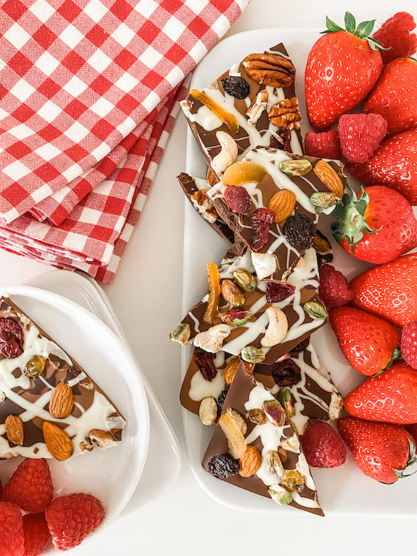 Triple Chocolate Fruit and Nut Bark on a square white plate with strawberries and raspberries and a checked napkin