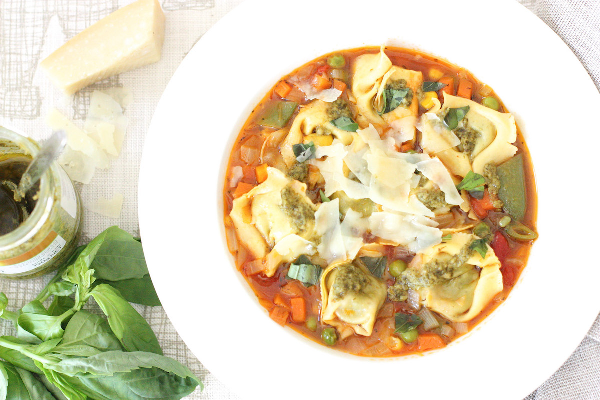 Big Hearty Pasta Soup in a white bowl with basil, Parmesan and pesto