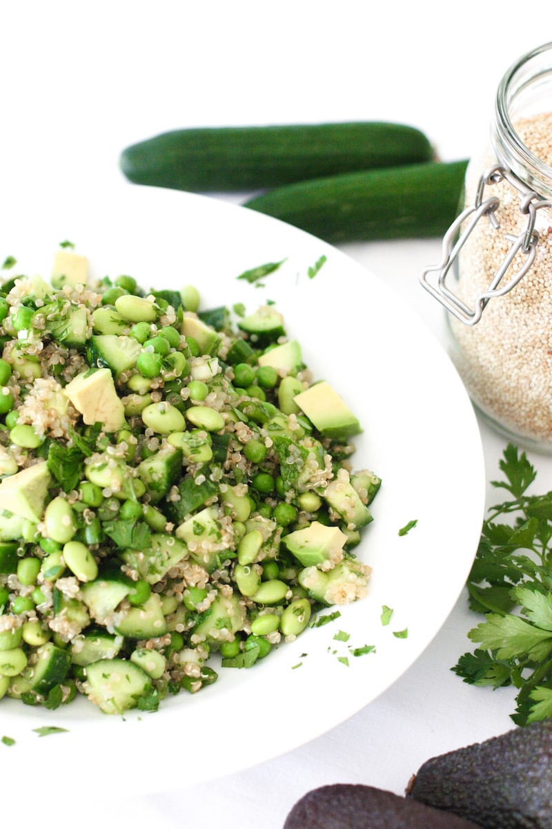 A quinoa salad with green herbs and vegetables in a white dish