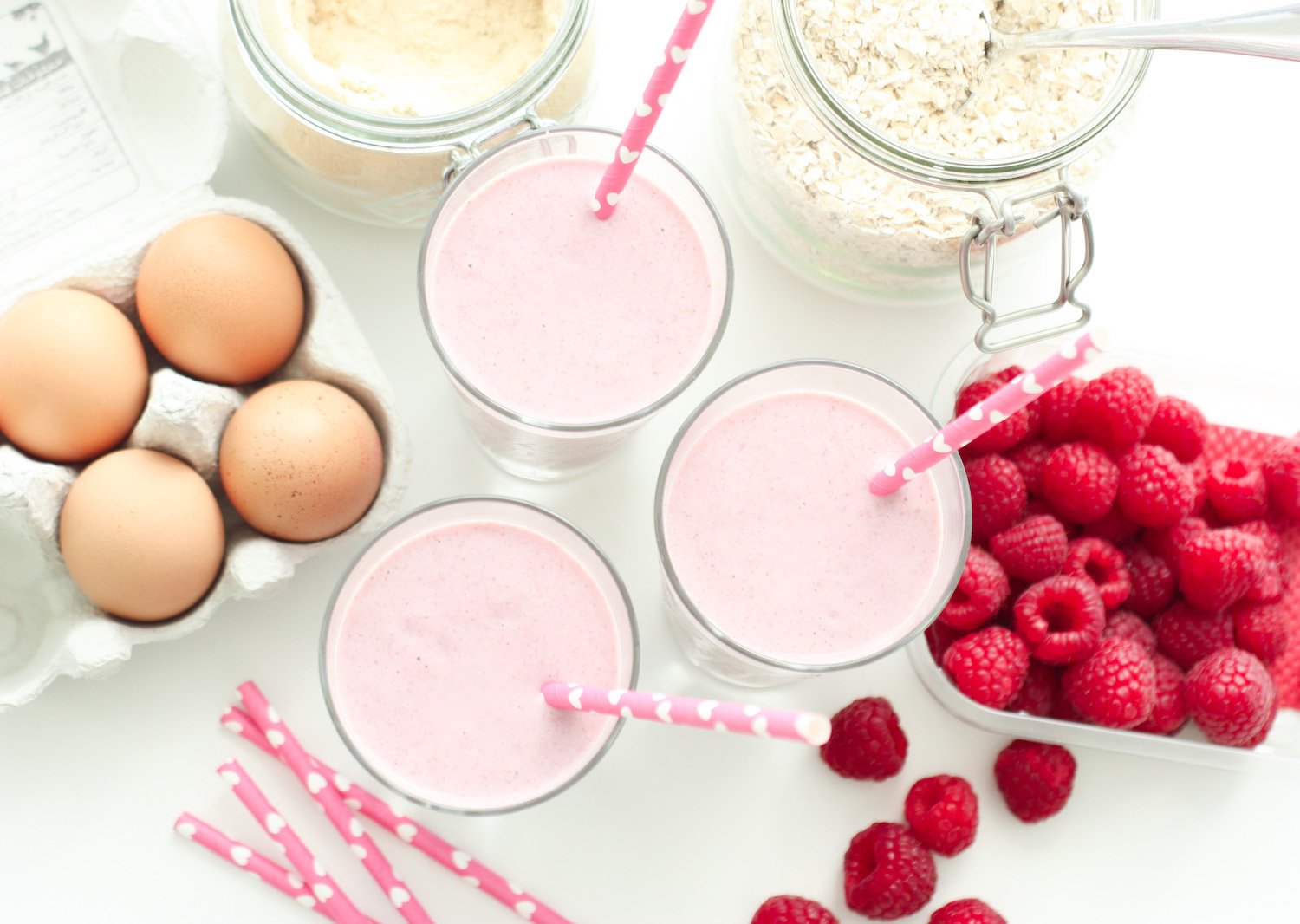 Raspberry Protein Shake in 3 glasses shot from above next to eggs, oats and raspberries