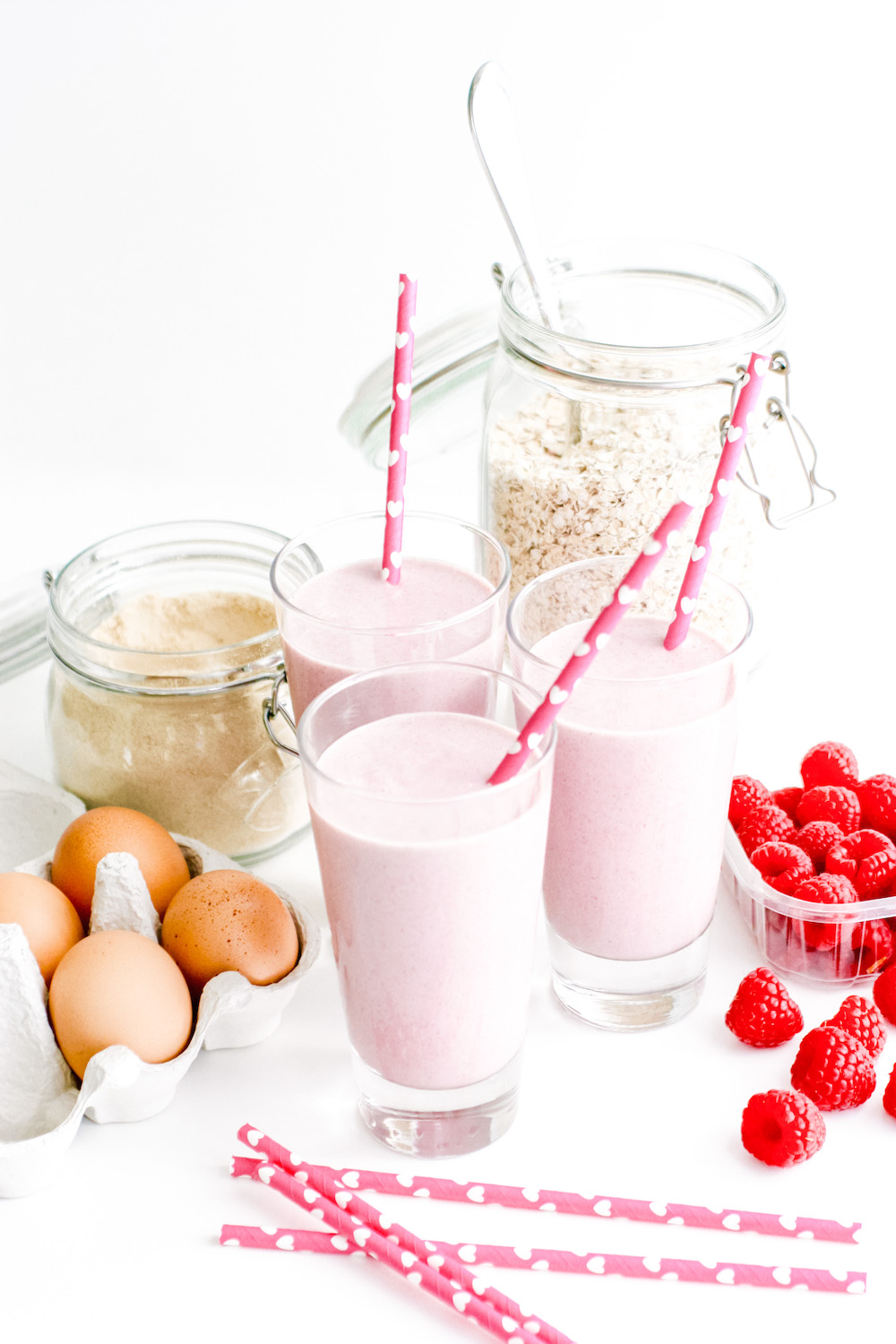 Raspberry Protein Shake in 3 glasses, next to eggs, oats and raspberries