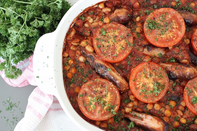 Sausage and Bean Hotpot in white baking dish, next to some curly parsley