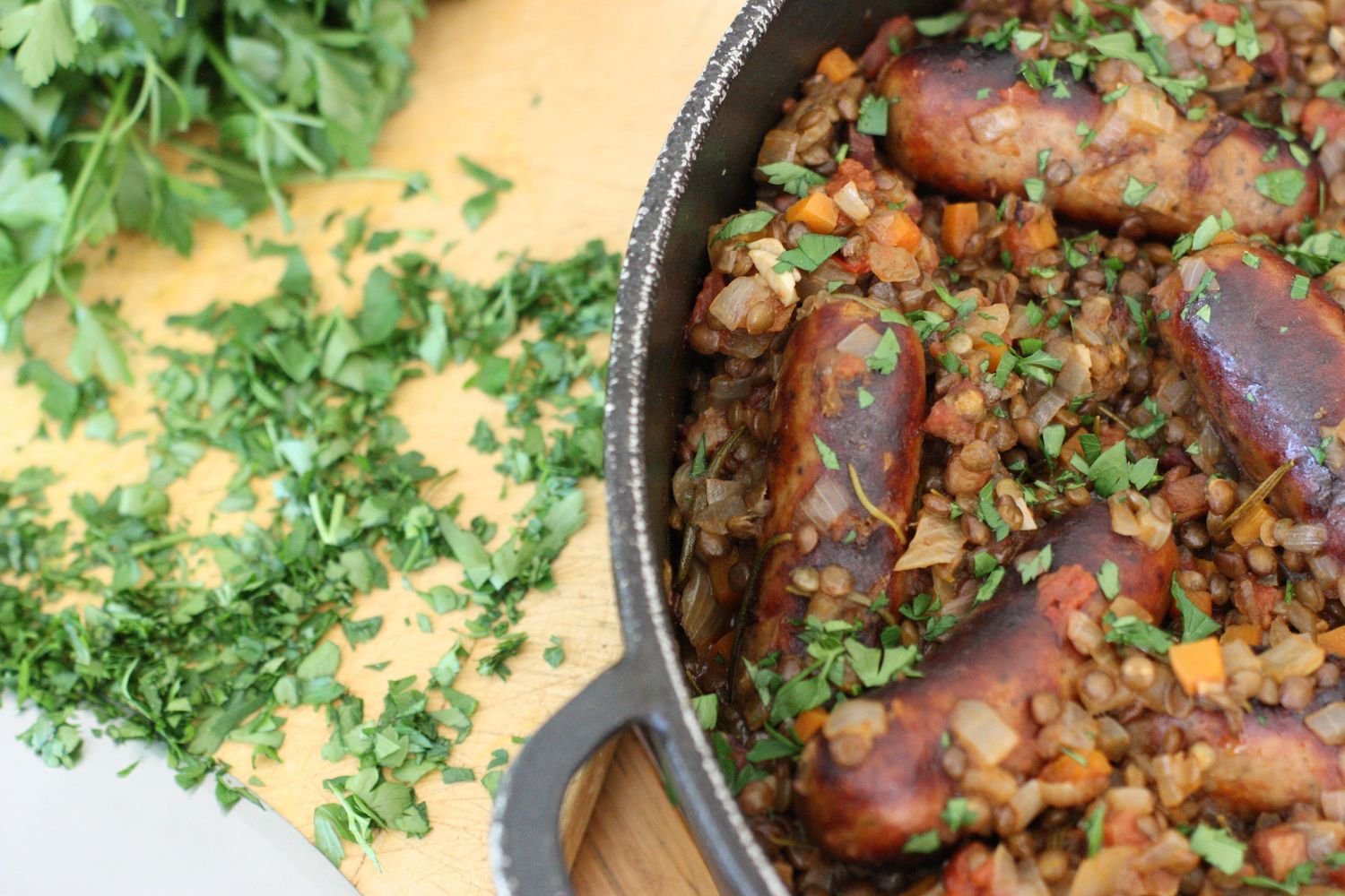 Sausage and Puy Lentil Pot in black pan sprinkled with fresh herbs
