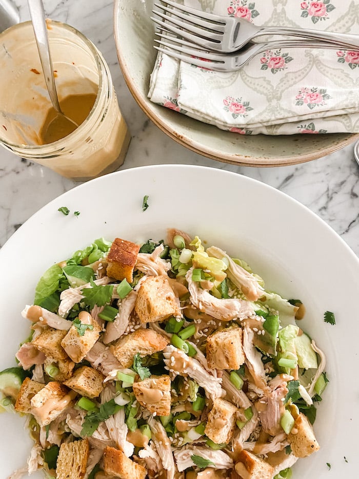 Delightful Summer Chicken Salad in white dish with dressing jar and plates for eating