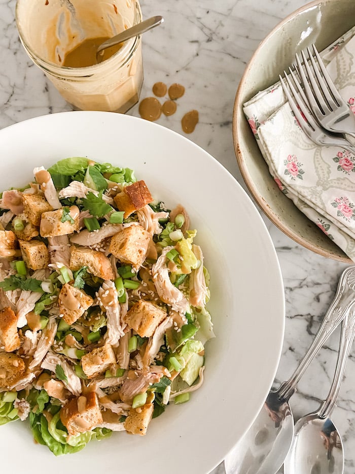 Delightful Summer Chicken Salad in white dish with serving cutlery and dressing
