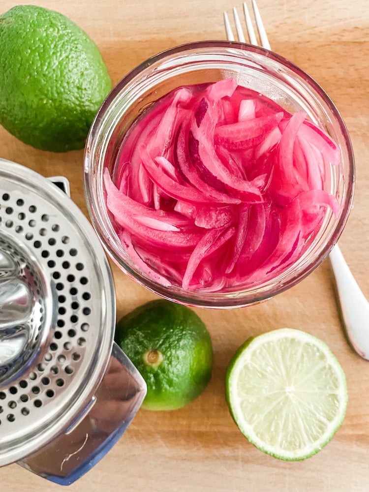 Pickled red onions in a jar with limes