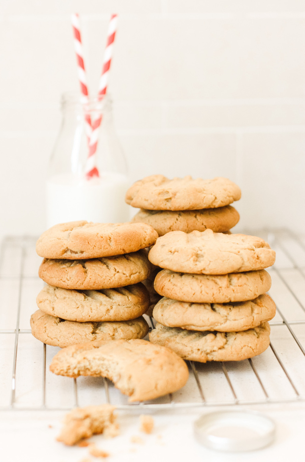 Piles of stem ginger cookies on a cooling rack with a small bottle of milk