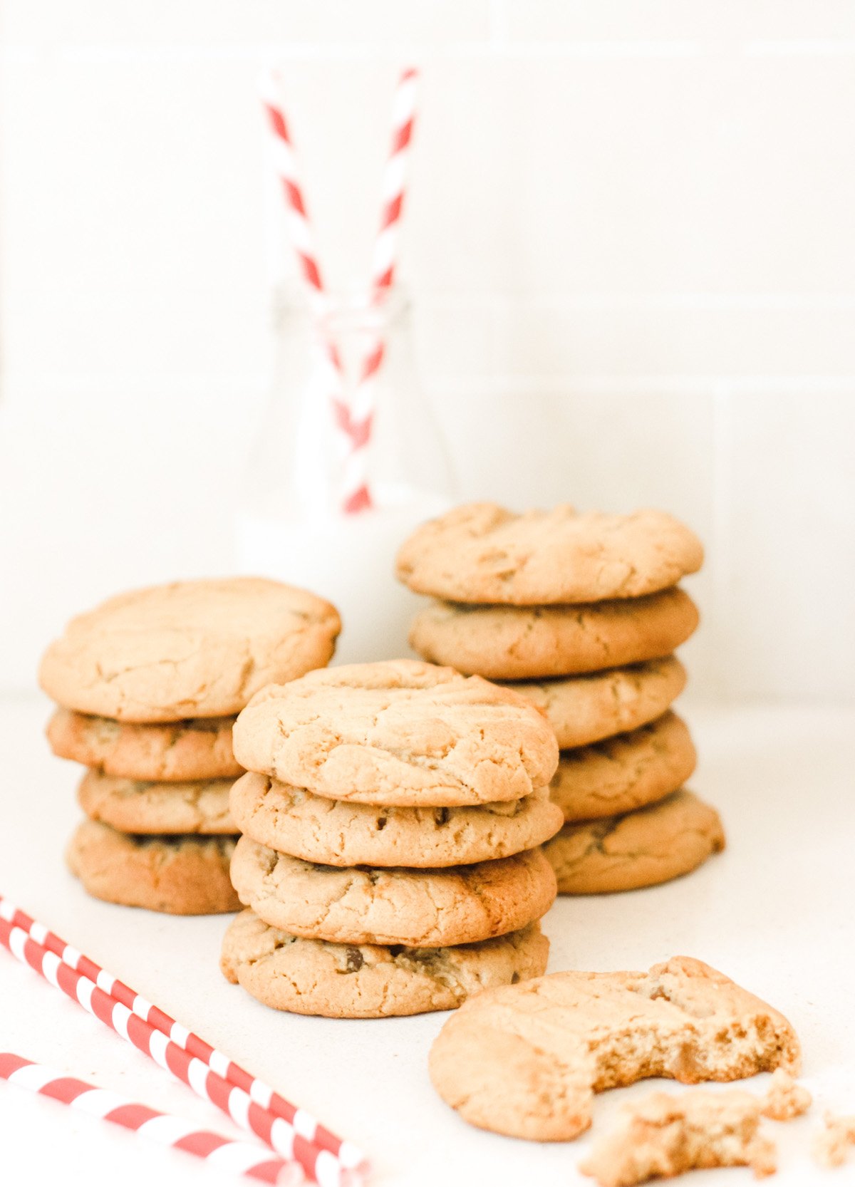 Stem ginger cookies in three piles with a bottle of milk and straws