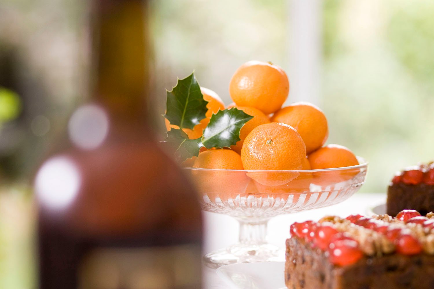 Glass bowl of satsumas with a bottle of sherry in the foreground