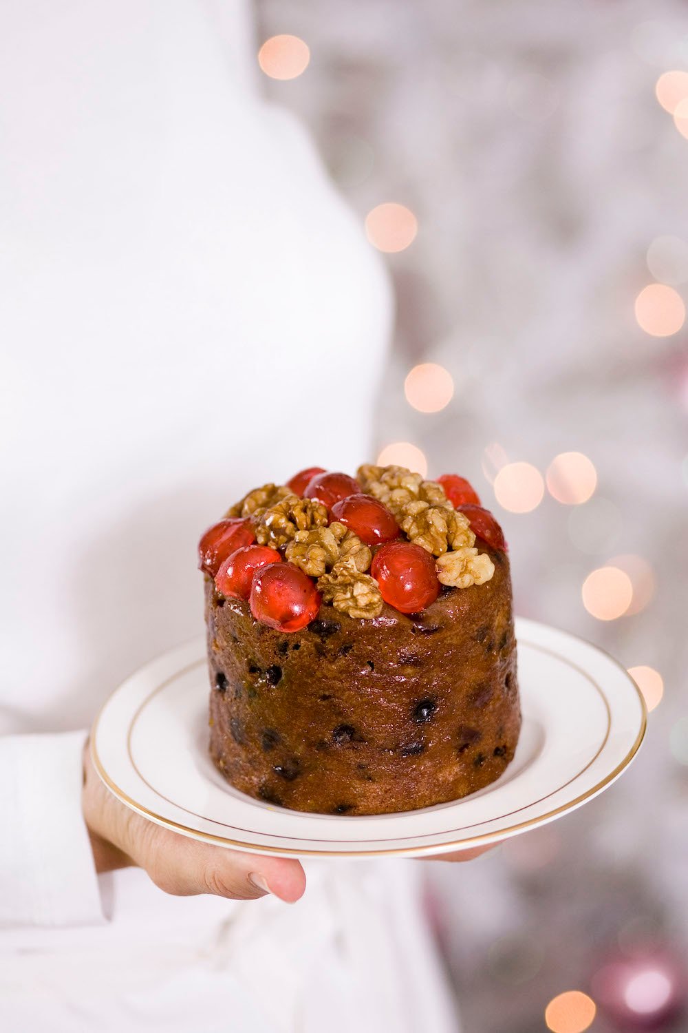 A small Christmas cake on a white plate held in front of sparkly lights