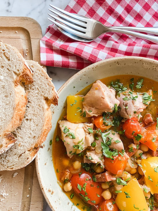 Chicken, Chorizo and Chickpea Stew in a green bowl with bread and a checked napkin