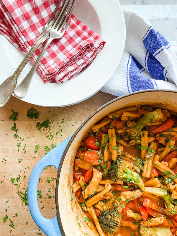 Chicken and Chorizo One Pot Pasta in a blue casserole dish and sitting on a wooden board