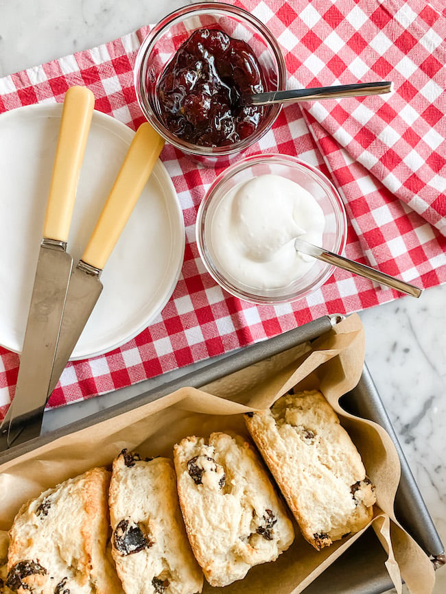 Fruit Scones in a tin, with a pot of cream and jam